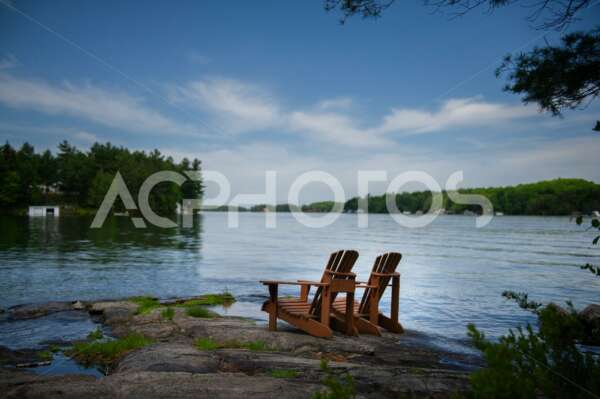 Adirondack chairs on a rock facing a lake 2696