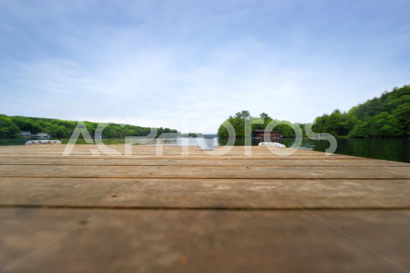 Metal coffee cup on a wooden dock facing a lake 3280