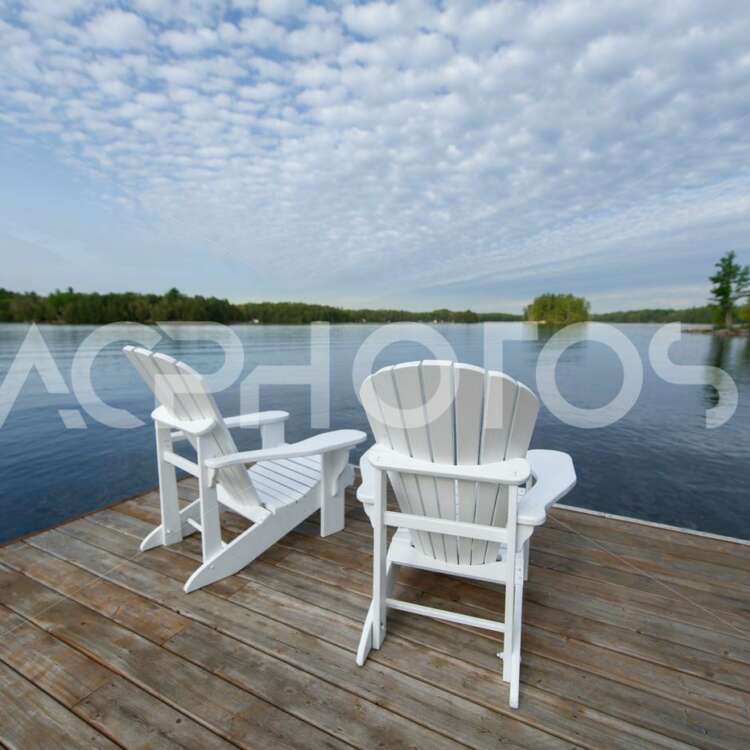 Two white Adirondack chairs on a lake in Ontario - GettaPix