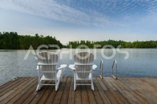 Two white Adirondack chairs on a wooden dock 3530