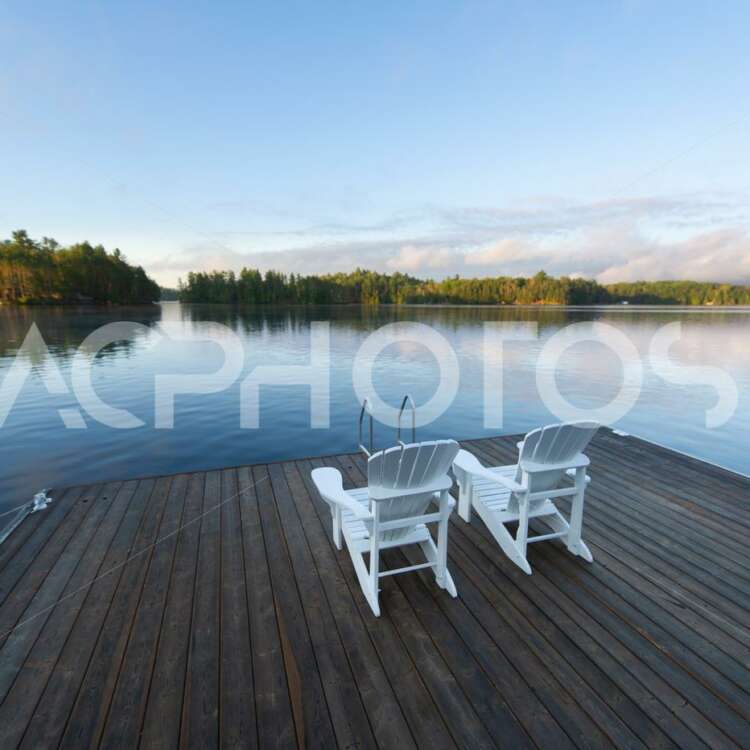 White Adirondack Chairs on a Wooden Dock on a Lake - GettaPix