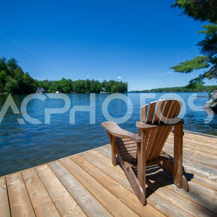 Adirondack chair on a wooden dock facing a lake in Muskoka - GettaPix