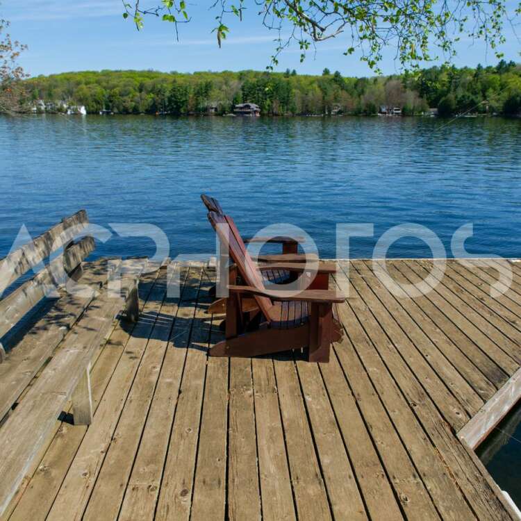 Two Adirondack chairs on a wooden dock facing a lake in Muskoka - GettaPix