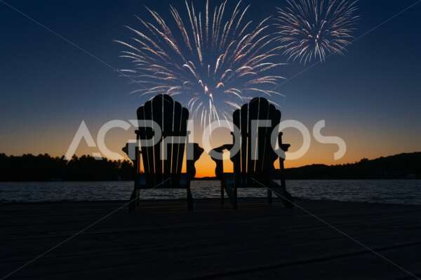 Two empty Adirondack chairs during fireworks on the lake - GettaPix