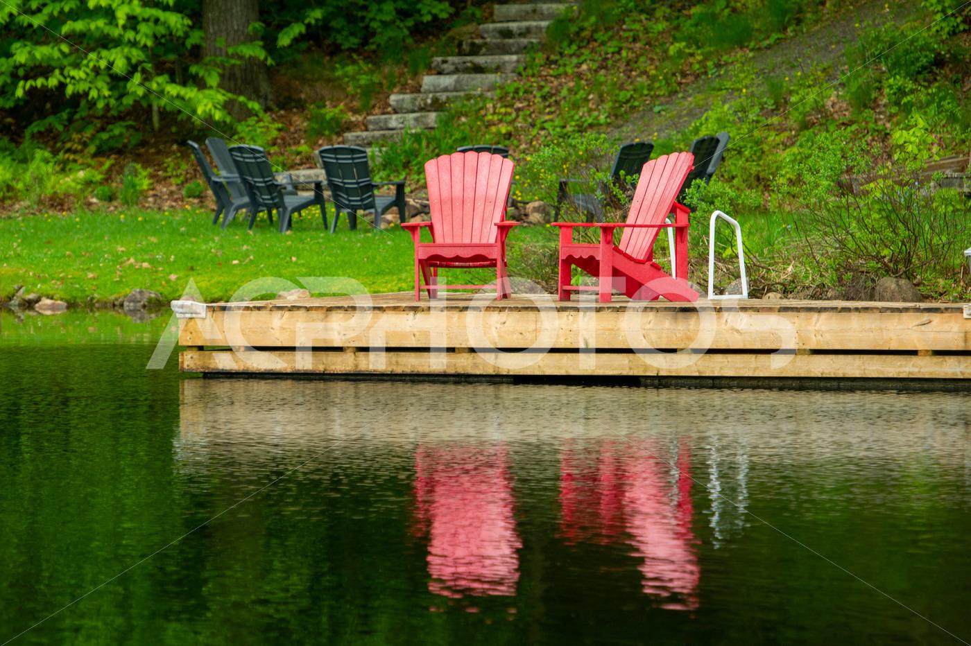 Two red Adirondack chairs on a cottage wookend dock - GettaPix