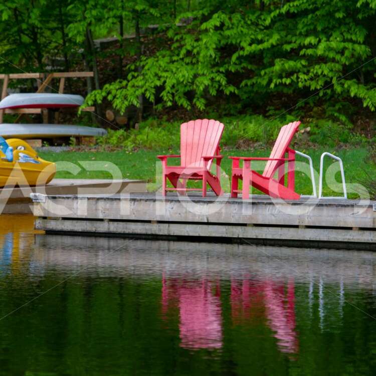 Two red Adirondack chairs reflecting on the water - GettaPix