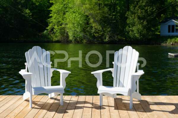 Two white Adirondack chairs on a wooden dock - GettaPix