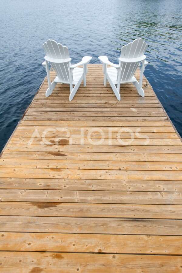 White Adirondack chairs facing a lake - GettaPix