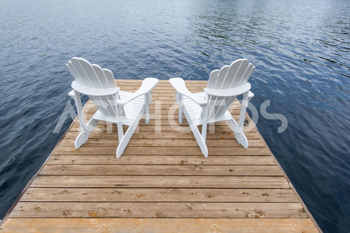 White Adirondack chairs on a pier facing a lake - GettaPix